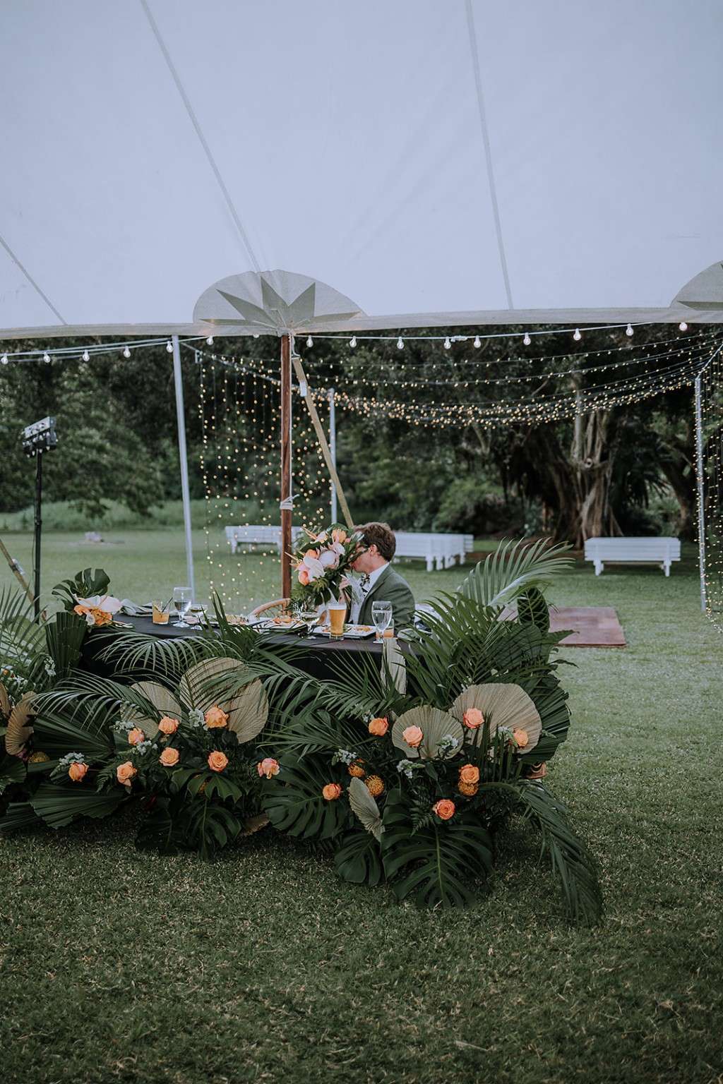 Green tropical reception decor beneath a white canopy